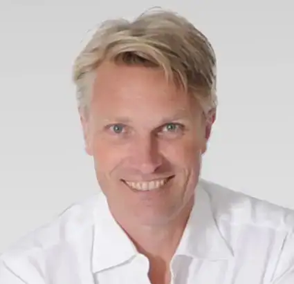 Ein lächelnder Mann mit blonden Haaren in einem weißen Hemd, der für die deutsche Möbelkampagne von Schultz Möbel posiert. Ein lächelnder Mann mit blonden Haaren in einem weißen Hemd, der für die deutsche Möbelkampagne von Schultz Möbel posiert.
